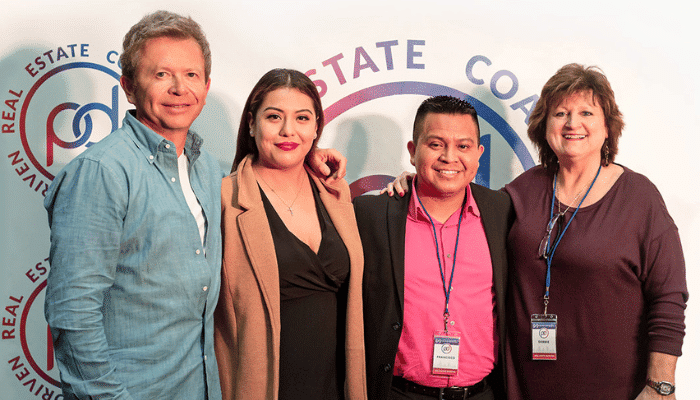 Peter Vekselman and Julie Muse, founders of Partner Driven, reflect on 5 successful years of teaching real estate investing. They are in a modern office setting with a wall displaying photos of successful house flips and happy clients, symbolizing the impact of their work.