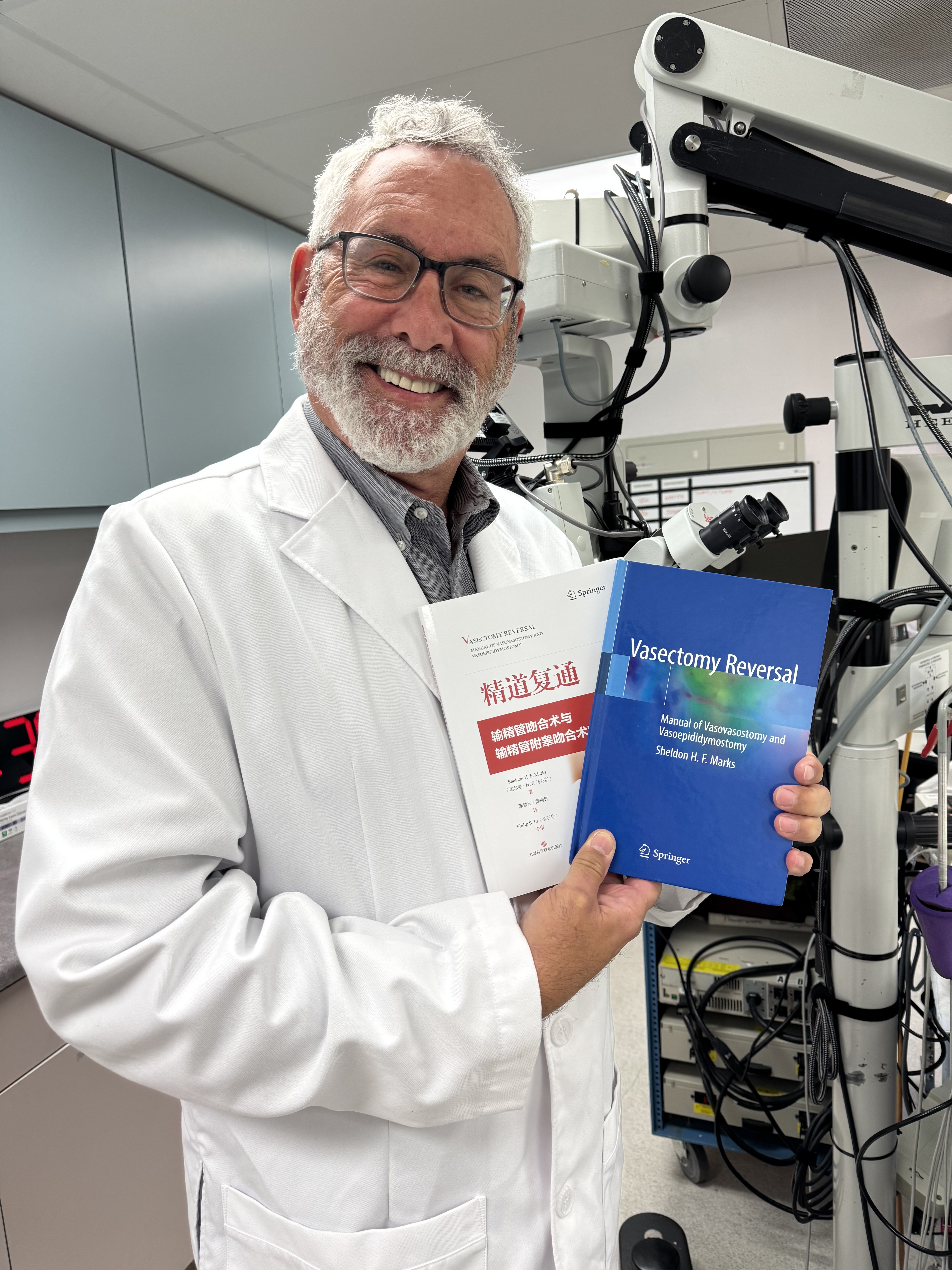 Dr. Sheldon Marks, vasectomy reversal expert and founder of ICVR, holding his Springer surgical textbooks on vasovasostomy and vasoepididymostomy, including the Chinese edition.