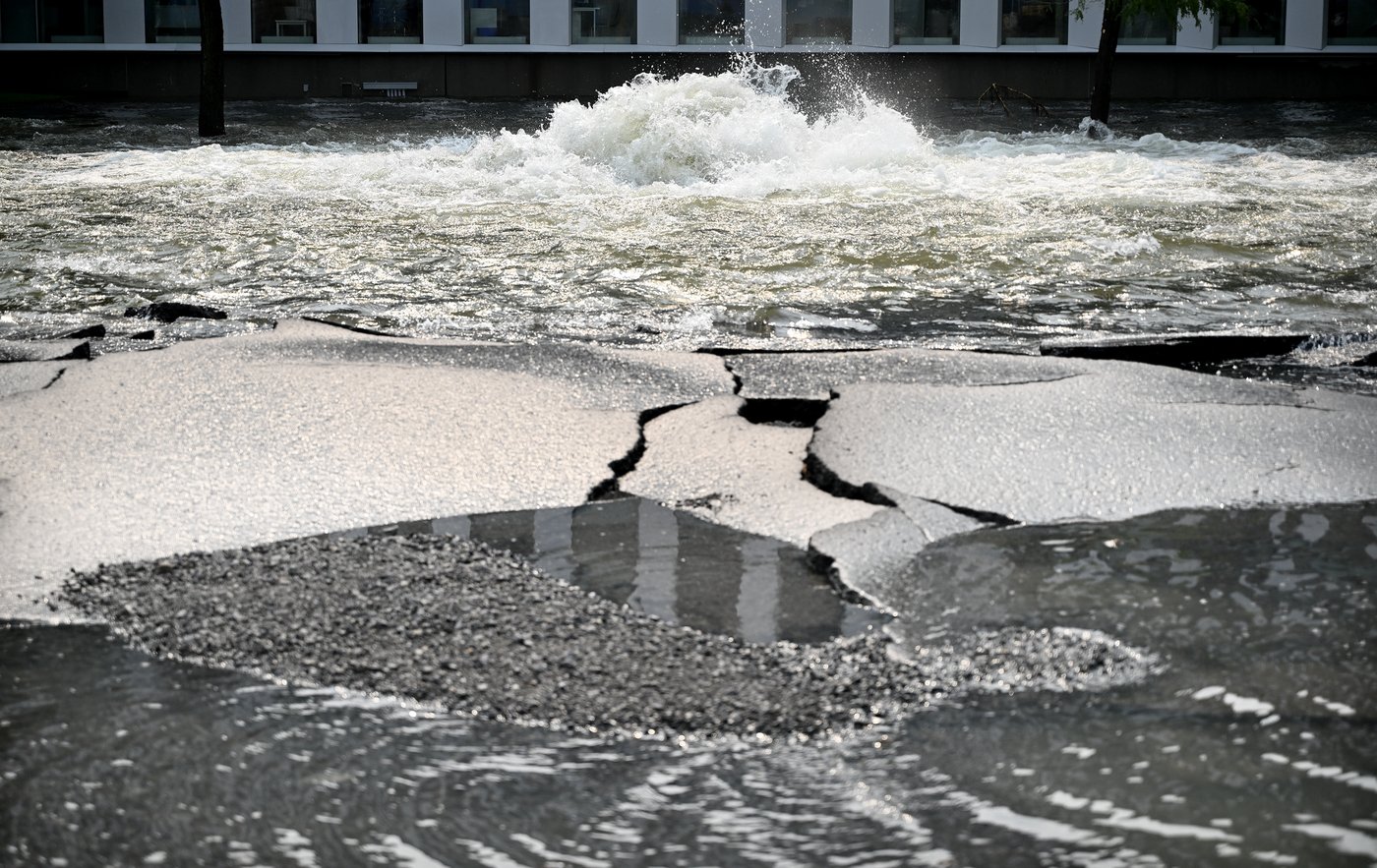 Cracked asphalt is shown next to a broken water main on a street in Montreal, Friday, Aug. 16, 2024, causing flooding in several streets of the area. THE CANADIAN PRESS/Graham Hughes