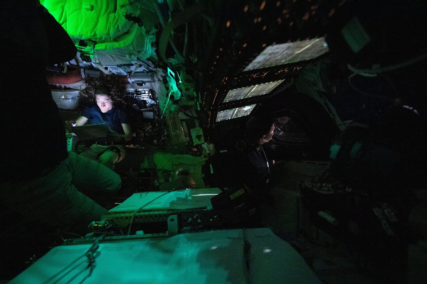 In this photo provided by NASA, astronaut Christina Koch, background left, is illuminated by a screen inside the darkened Orion spacecraft Integrity on the third day of the Artemis II mission, Friday, April 3, 2026. At right, Canadian Space Agency astronaut Jeremy Hansen looks out of one of Orion's windows. (NASA via AP)
