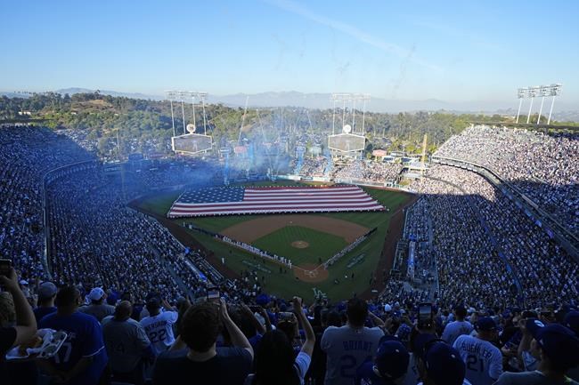 An American flag covers the outfield during the national anthem before Game 1 of the baseball World Series, Friday, Oct. 25, 2024, in Los Angeles. (AP Photo/Julio Cortez)