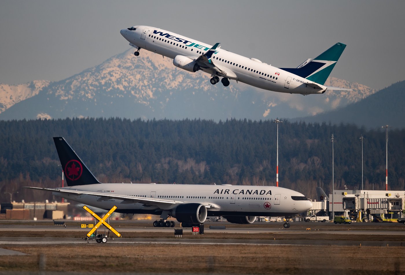 An Air Canada flight departing for Toronto, bottom, taxis to a runway as a WestJet flight bound for Palm Springs takes off at Vancouver International Airport, in Richmond, B.C., on Friday, March 20, 2020. THE CANADIAN PRESS/Darryl Dyck