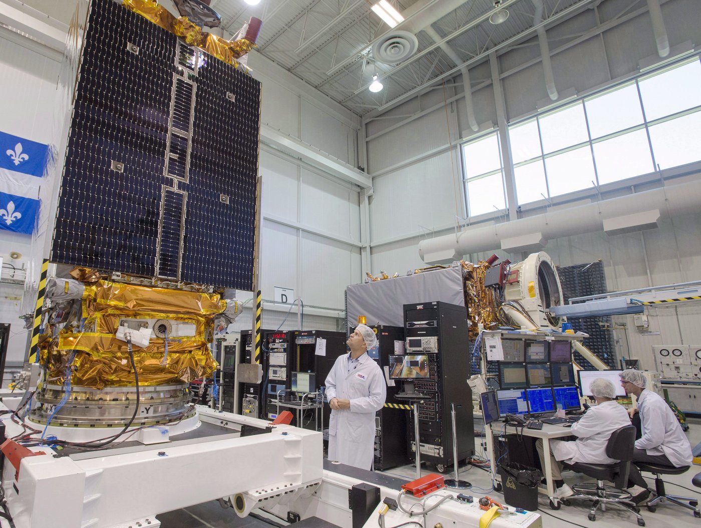 Jean-Michel Leclerc, centre, lead engineer of the Radarsat Constellation Mission is seen with two of the three satellites at the MDA facility Thursday, June 21, 2018 in Montreal. THE CANADIAN PRESS/Ryan Remiorz