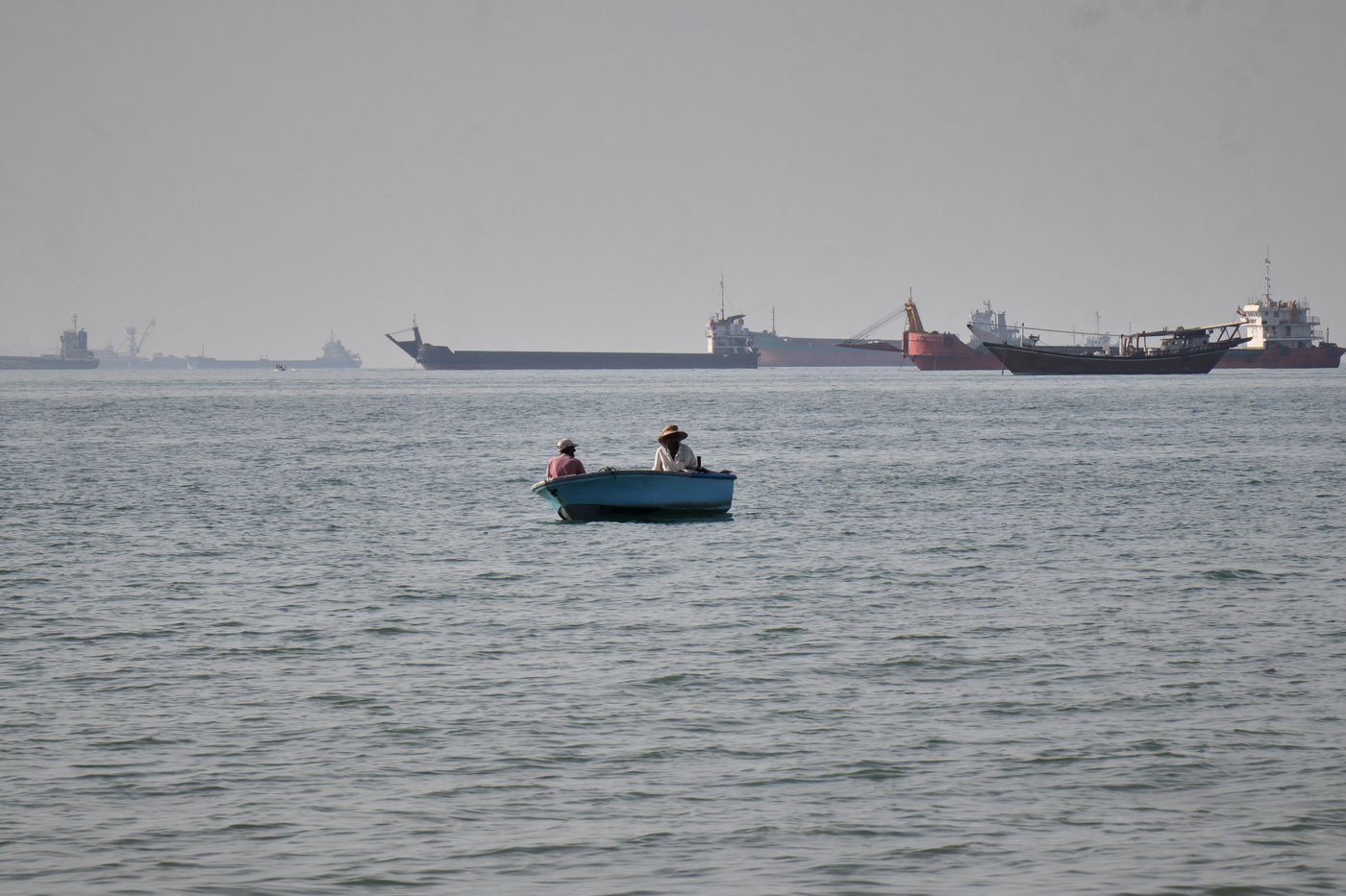 Two men sit in a small boat on the water as a mix of bulk carriers, cargo ships, and service vessels line the horizon in the Strait of Hormuz off Bandar Abbas, Iran, Monday, April 27, 2026.(Razieh Poudat/ISNA via AP)