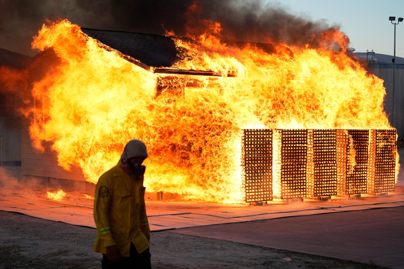 A wildfire researcher walks in front of an accessory dwelling unit burning during an experiment at the Institute for Business & Home Safety center on Thursday, April 16, 2026, in Richburg, S.C. (AP Photo/Erik Verduzco)