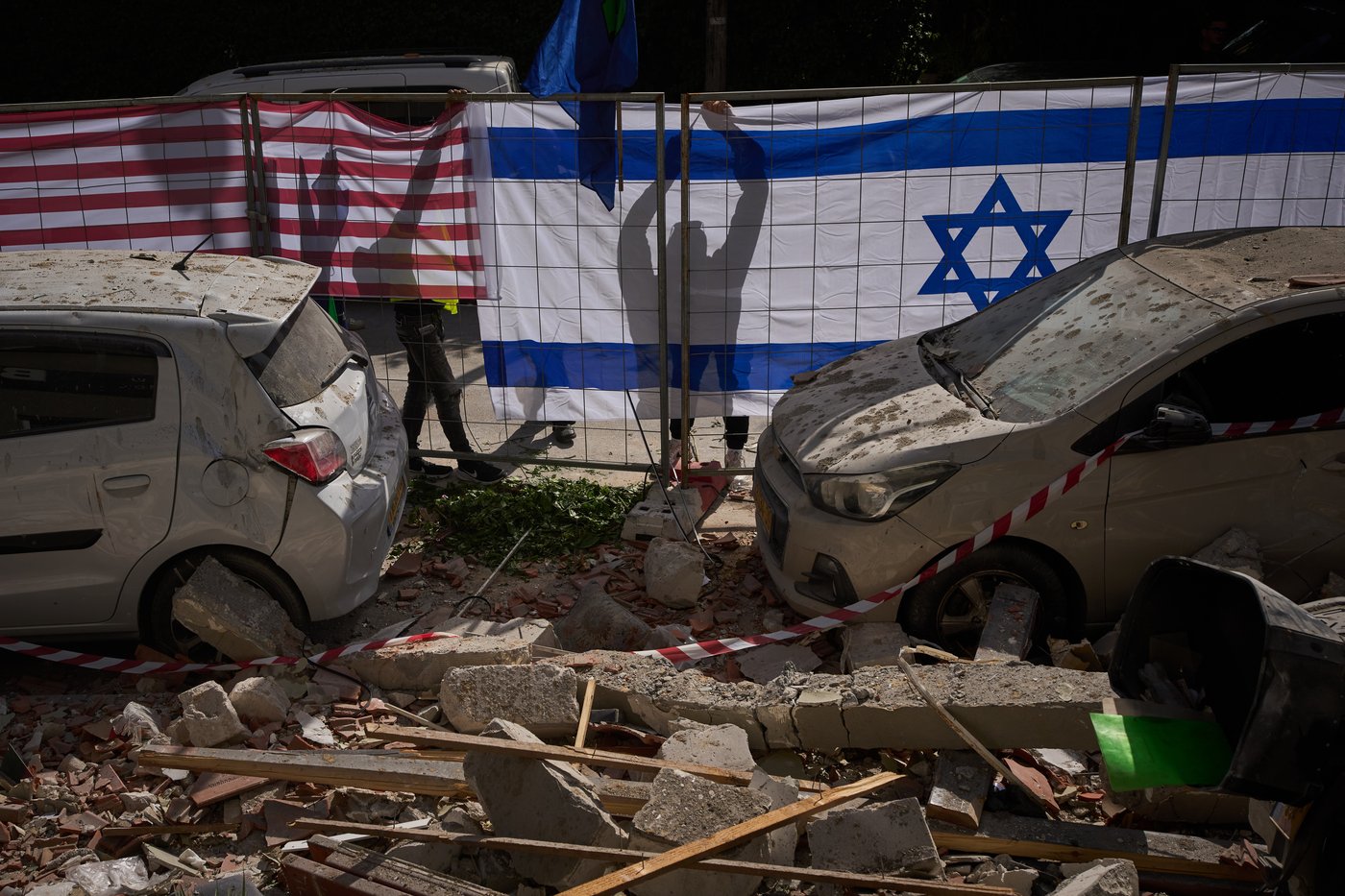 Israeli authorities hang Israeli and U.S. flags at the site struck by an Iranian missile that killed two people, in Ramat Gan, Israel, Wednesday, March 18, 2026. (AP Photo/Oded Balilty)