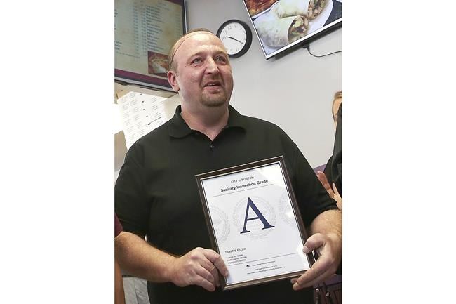 FILE - Stavros Papantoniadis, owner of Stash's Pizza, a Boston sanitary grade certificate after inspection by the Health Division of the Inspectional Services Department on Nov 2, 2016, in Boston. (Pat Greenhouse/The Boston Globe via AP, File)