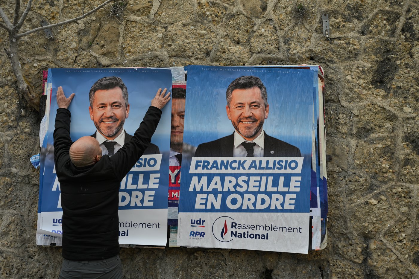 A supporter of far-right candidate Franck Allisio, pastes an electoral poster ahead of the first round of the mayoral elections, in Marseille, south of France, Friday, March 6, 2026. (AP Photo/Philippe Magoni)