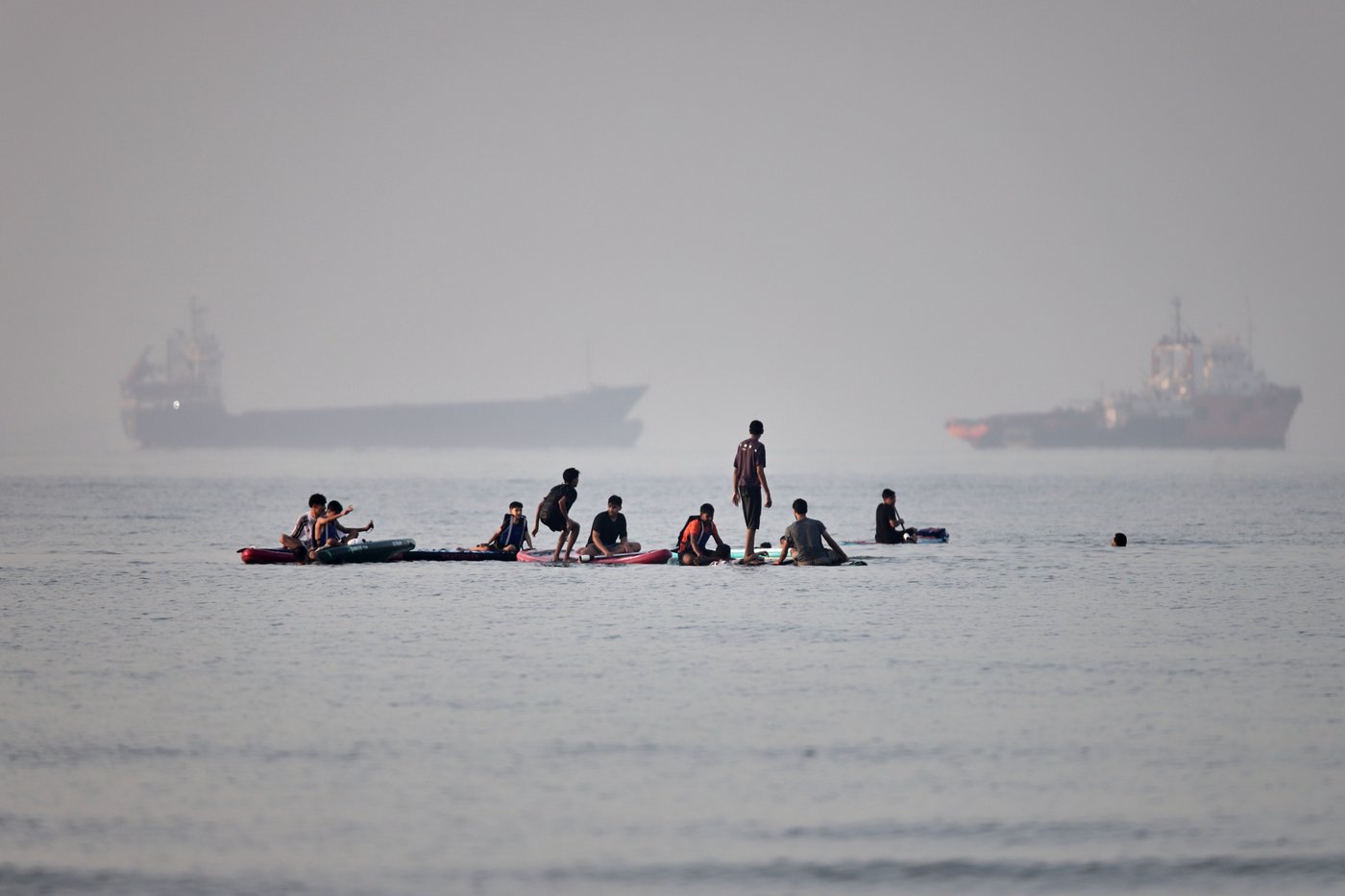 People gather on paddleboards in shallow water as cargo and service vessels are anchored in the Strait of Hormuz off Bandar Abbas, Iran, Monday, June 1, 2026. (Amirhosein Khorgooi/ISNA via AP)