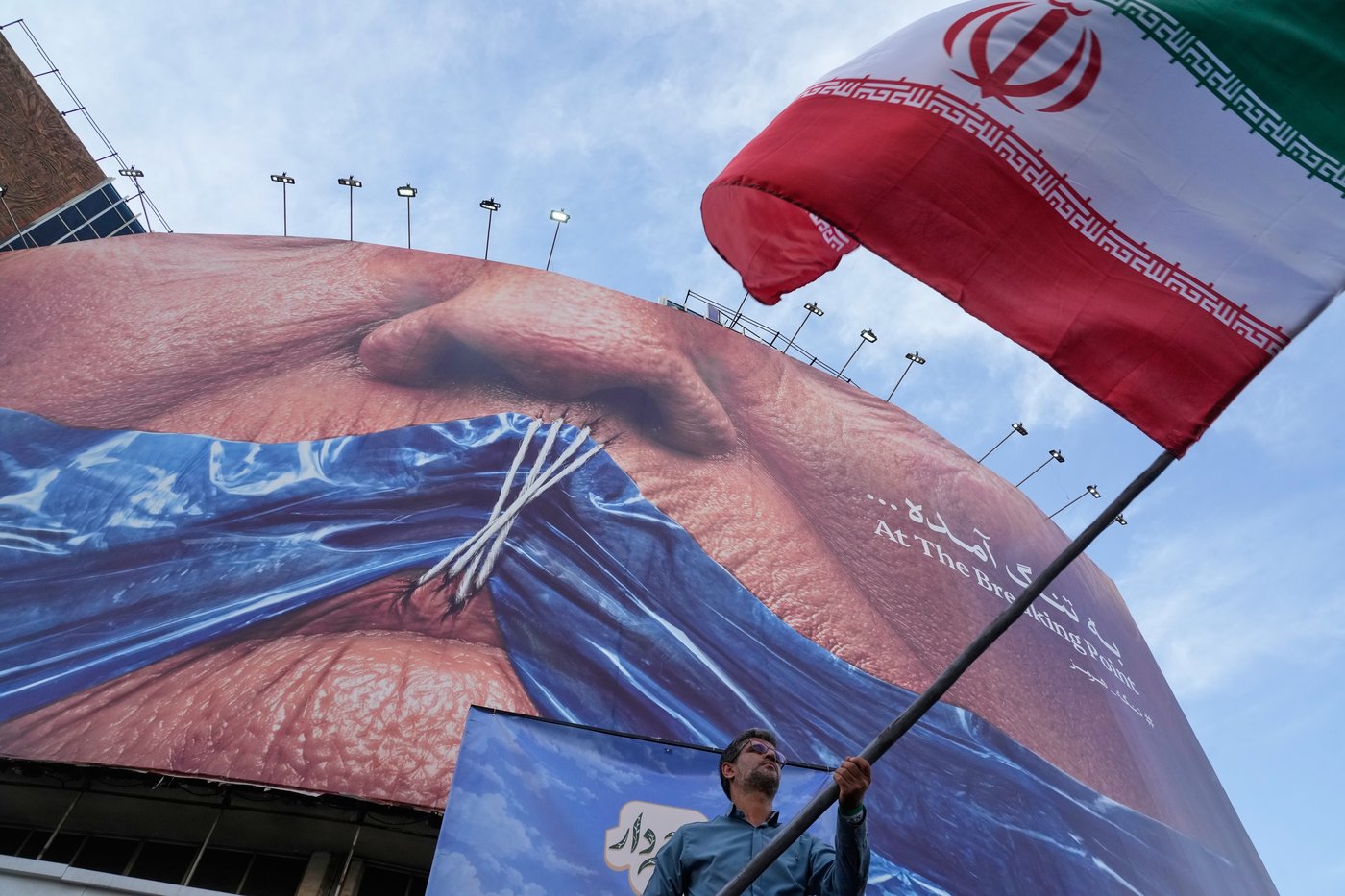 A man waves an Iranian flag for a pro-government campaign under a billboard with graphic showing Strait of Hormuz and sewn lips of U.S. President Donald Trump in a square in downtown Tehran, Iran, Wednesday, May 6, 2026. (AP Photo/Vahid Salemi)