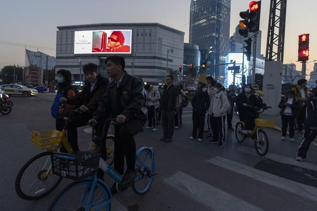 Pedestrians and cyclists wait to cross a traffic junction near a advertisement for iPhones in Beijing, Wednesday, Nov. 6, 2024. (AP Photo/Ng Han Guan)
