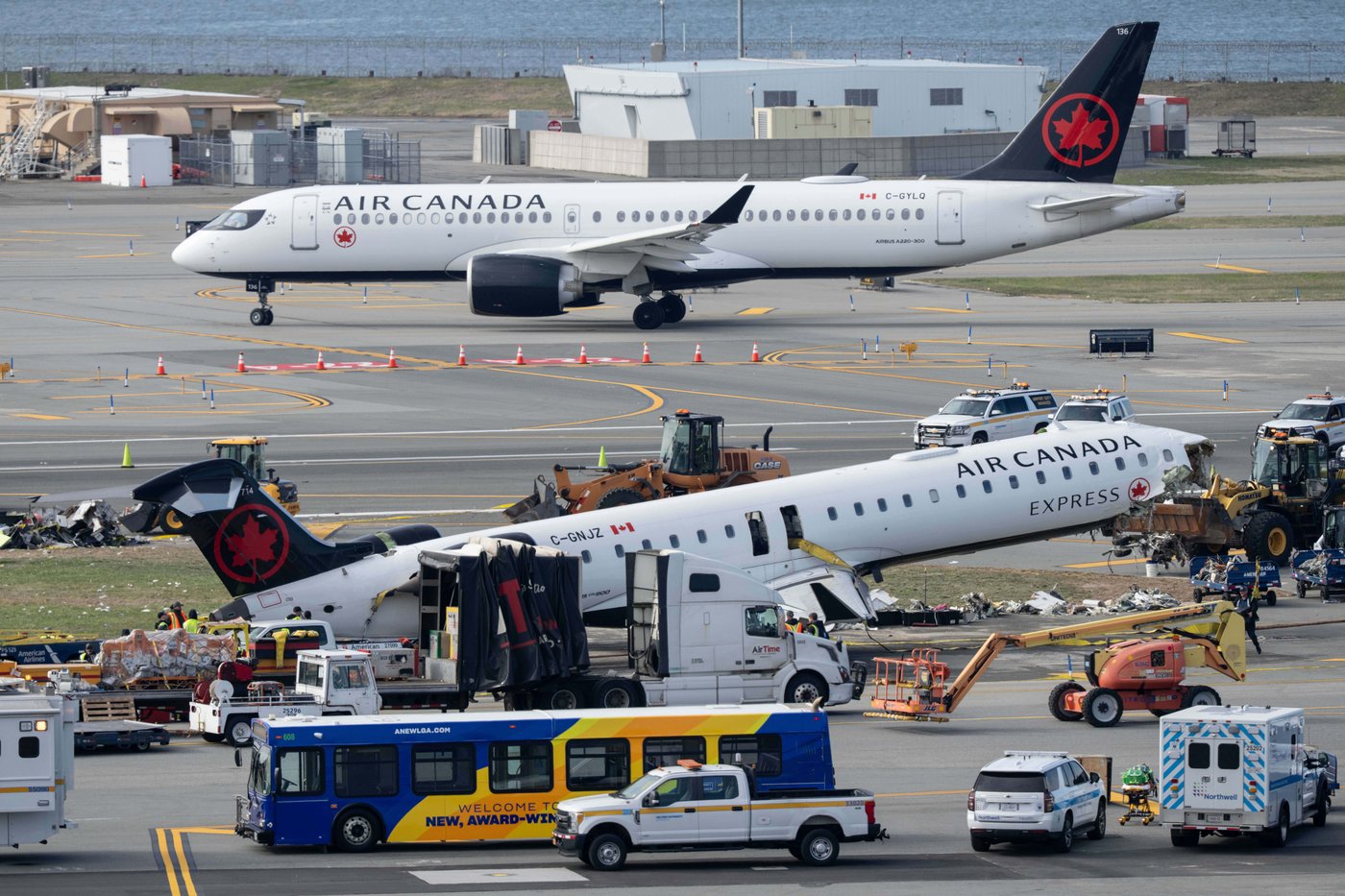 An Air Canada Express jet taxis past the wreckage of an Air Canada Express jet, Wednesday, March 25, 2026, as maintenance crews prepare to move the plane from the runway where it had collided with a Port Authority fire truck Sunday night at LaGuardia Airport, in New York. (AP Photo/Yuki Iwamura)