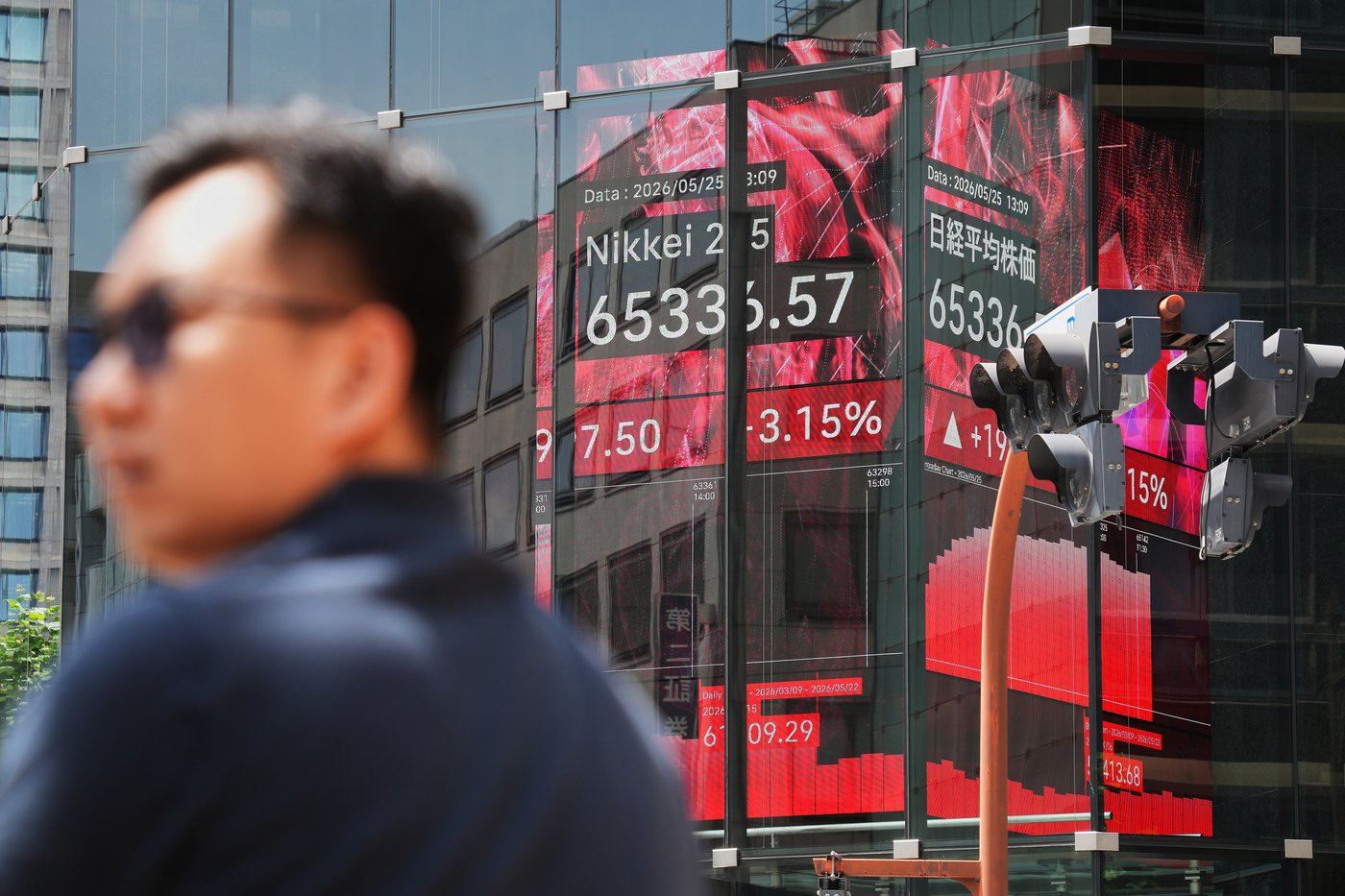 A person stands in front of an electronic stock board showing Japan's Nikkei index, seen through the glass wall of an office building Monday, May 25, 2026, in Tokyo. (AP Photo/Eugene Hoshiko)