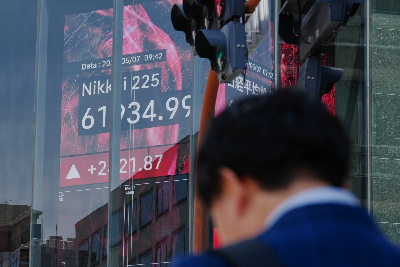 FILE - A person stands in front of an electronic stock board showing Japan's Nikkei index, seen through the glass wall of an office building in Tokyo, May 7, 2026. (AP Photo/Eugene Hoshiko, File)