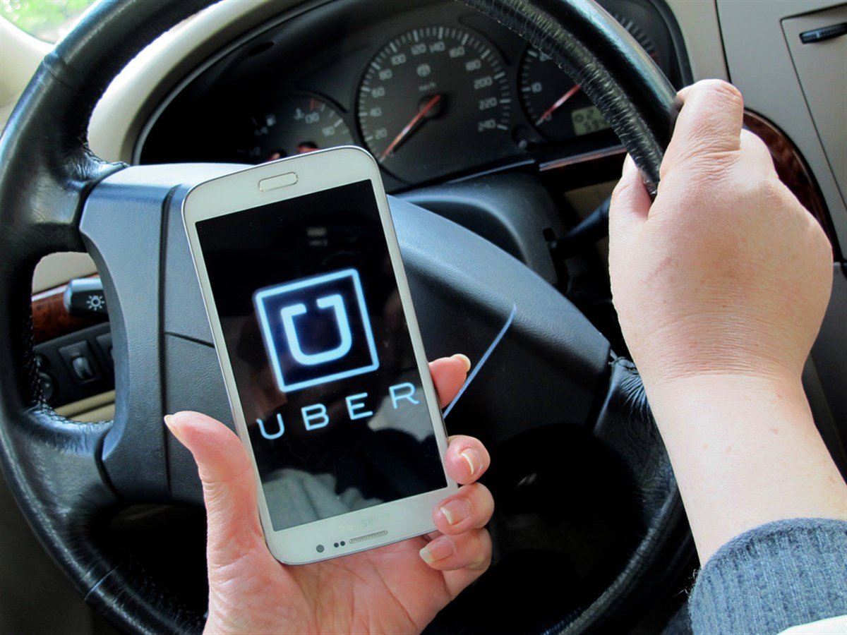 Photo of a person sitting in the drivers seat holding a smartphone with the Uber logo