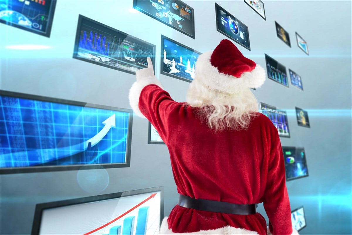Santa Claus pointing at screens with stock market data.