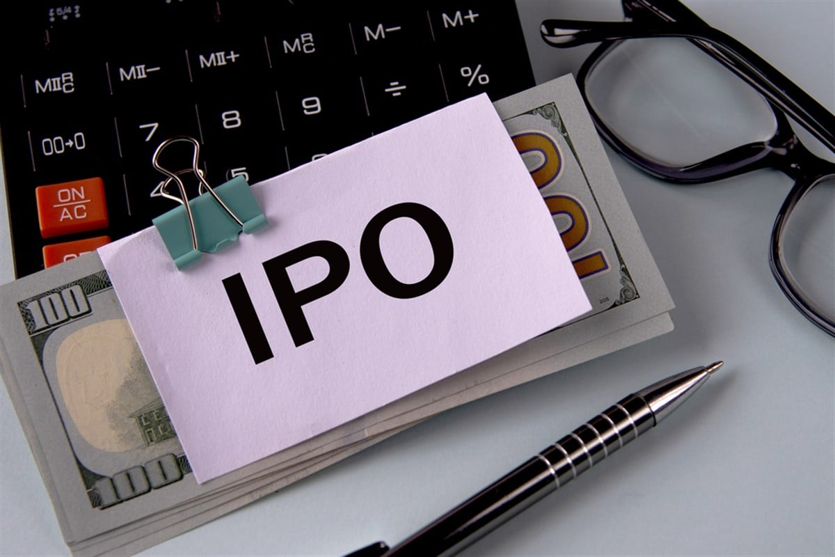 IPO (Initial public offering) - acronym on a white piece of paper fixed on banknotes against the background of a calculator, glasses and pen. Business and finance concept