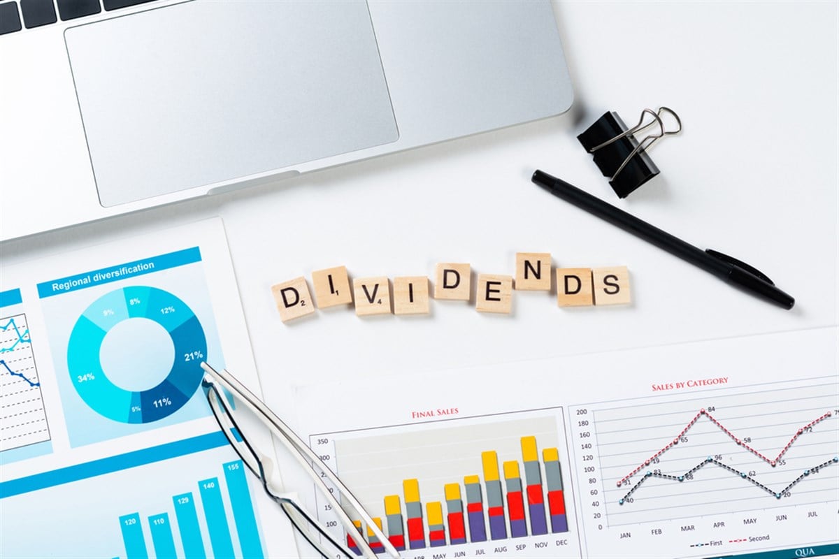 Phot of dividends payment concept with letters on wooden cubes. Still life of office workplace with supplies. Flat lay white surface with laptop computer and financial diagrams. Capital savings and investment
