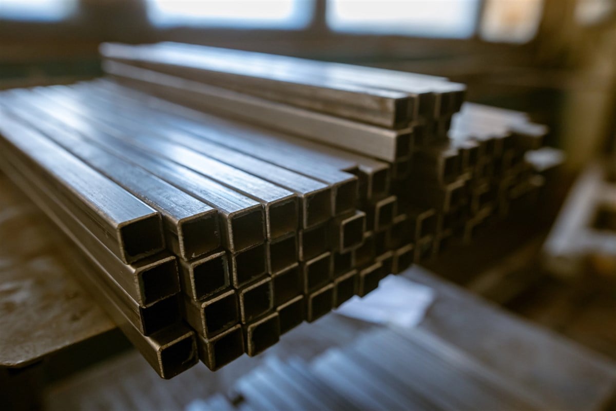 A neatly stacked pile of square metal tubes rests on a workbench in a workshop environment, ready for fabrication or use.