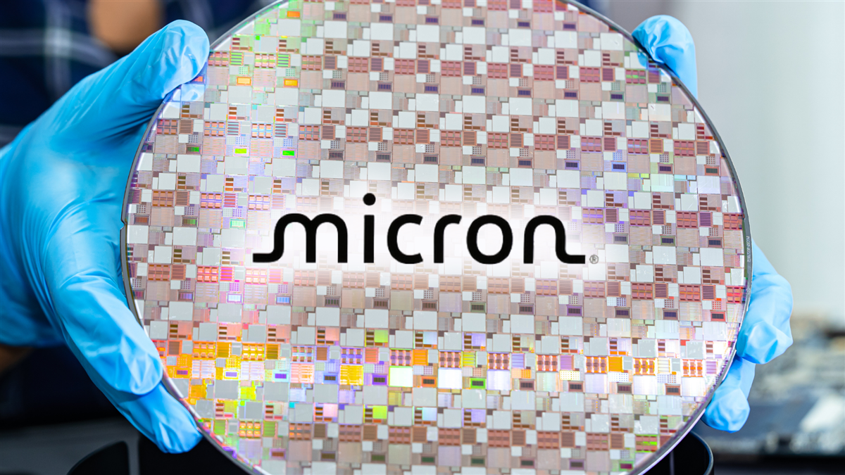 Alt Text Creator said: Gloved hands hold a Micron-branded semiconductor wafer featuring dense chip patterns, highlighting advanced memory manufacturing and tech-sector production.