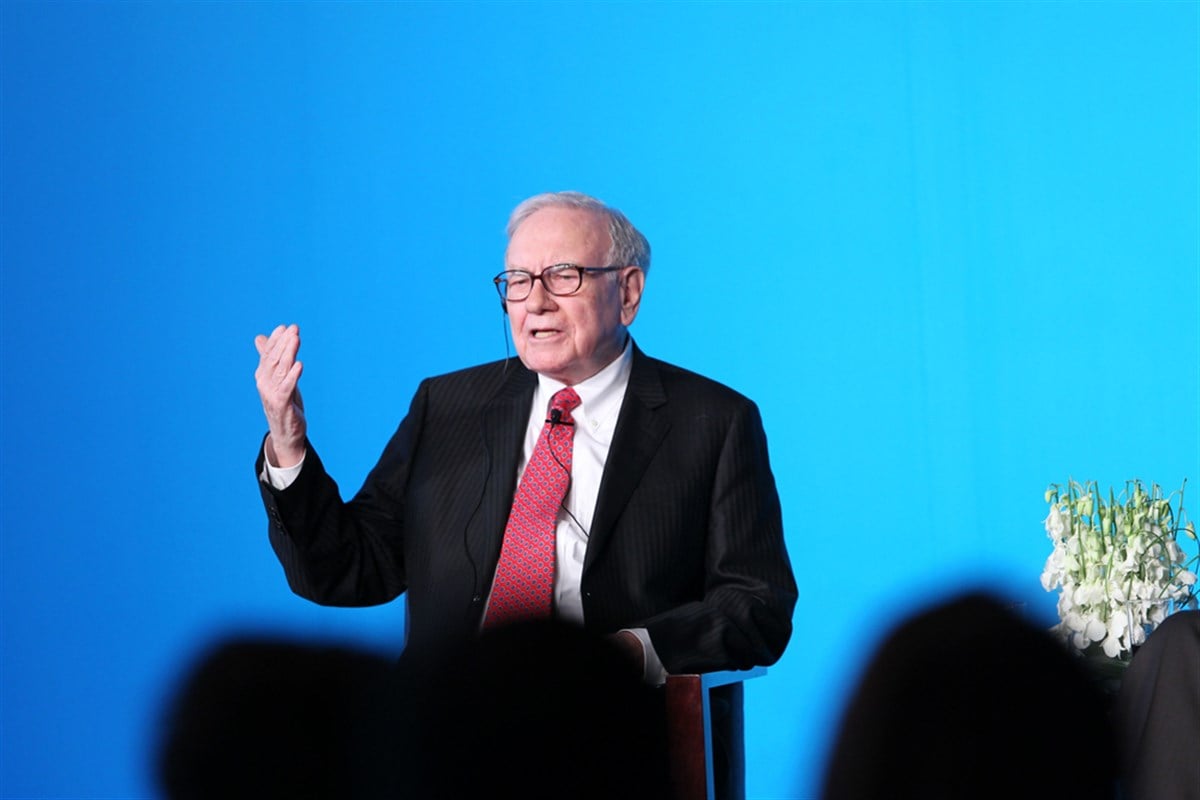 Warren Buffett, in a dark suit and red tie, appears onstage at a finance event; Berkshire Hathaway, made major Q3 portfolio changes.