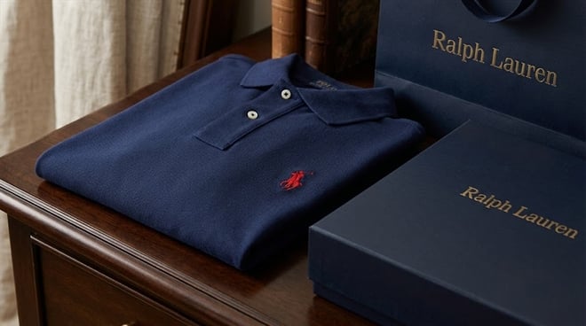 A folded navy blue Ralph Lauren polo shirt next to a branded box and shopping bag on a wooden table.