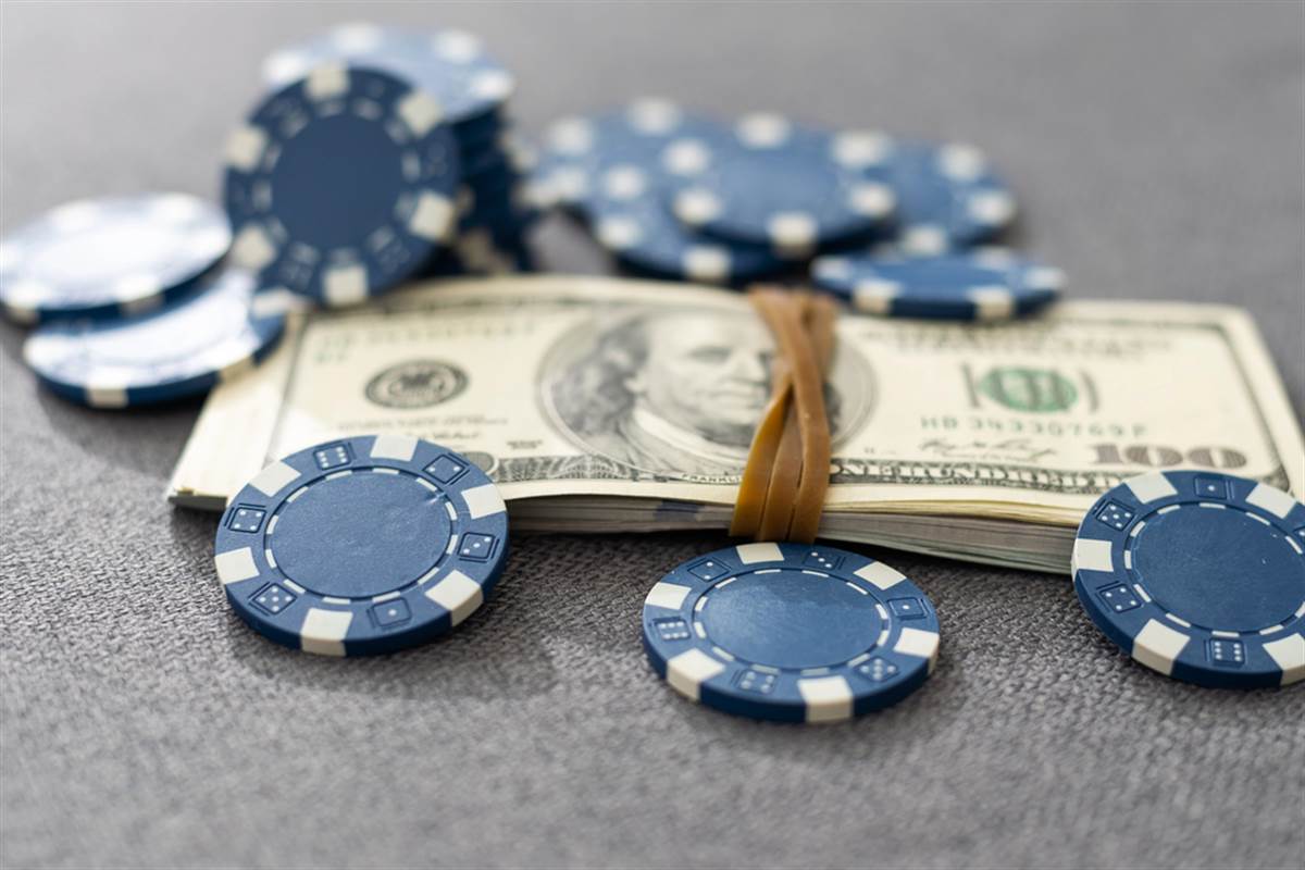 Blue casino chips scattered around a stack of $100 bills symbolize high-risk, high-reward blue-chip stock investing.