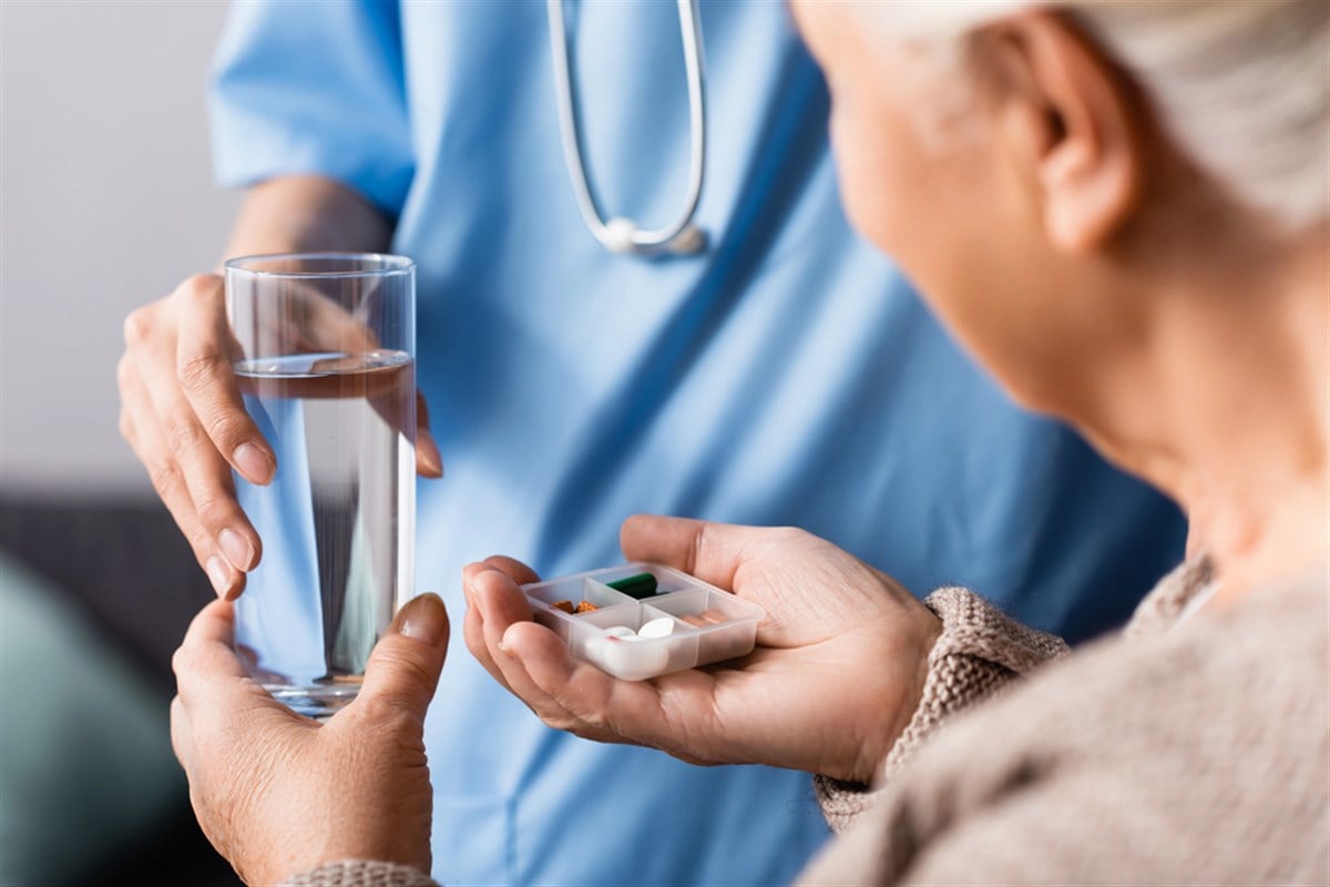 Partial view of nurse giving pills and glass of water to elderly woman.