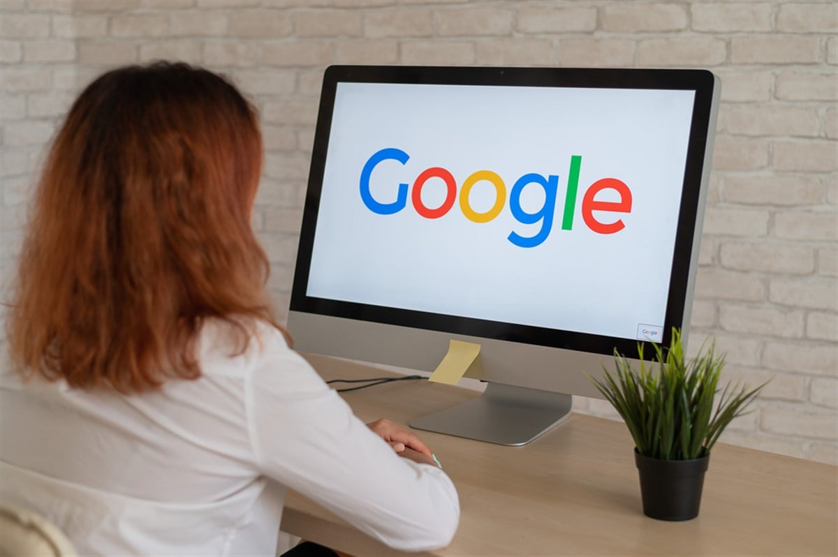 A woman sits at a computer with a Google logo on the monitor.