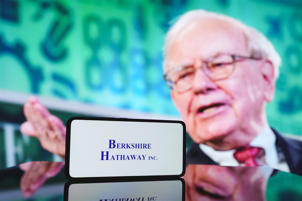 Berkshire Hathaway logo on smartphone in front of photo of Warren Buffett.