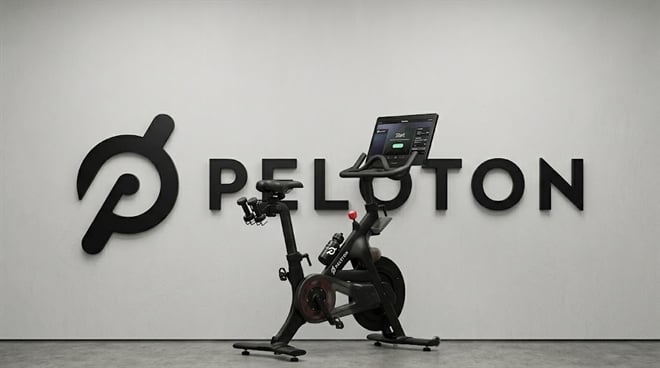 A Peloton stationary bike with an attached touchscreen display positioned in front of the Peloton logo.