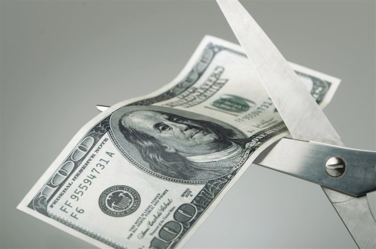 Scissors cutting $100 bill in half