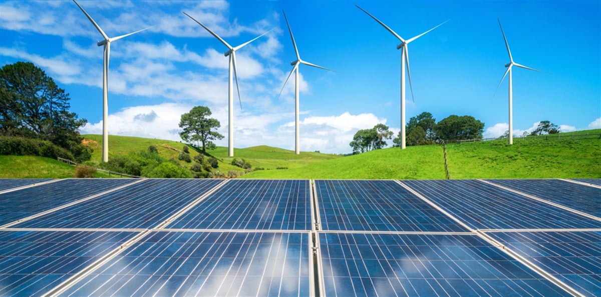 Solar panel and wind turbines farm on green hills.