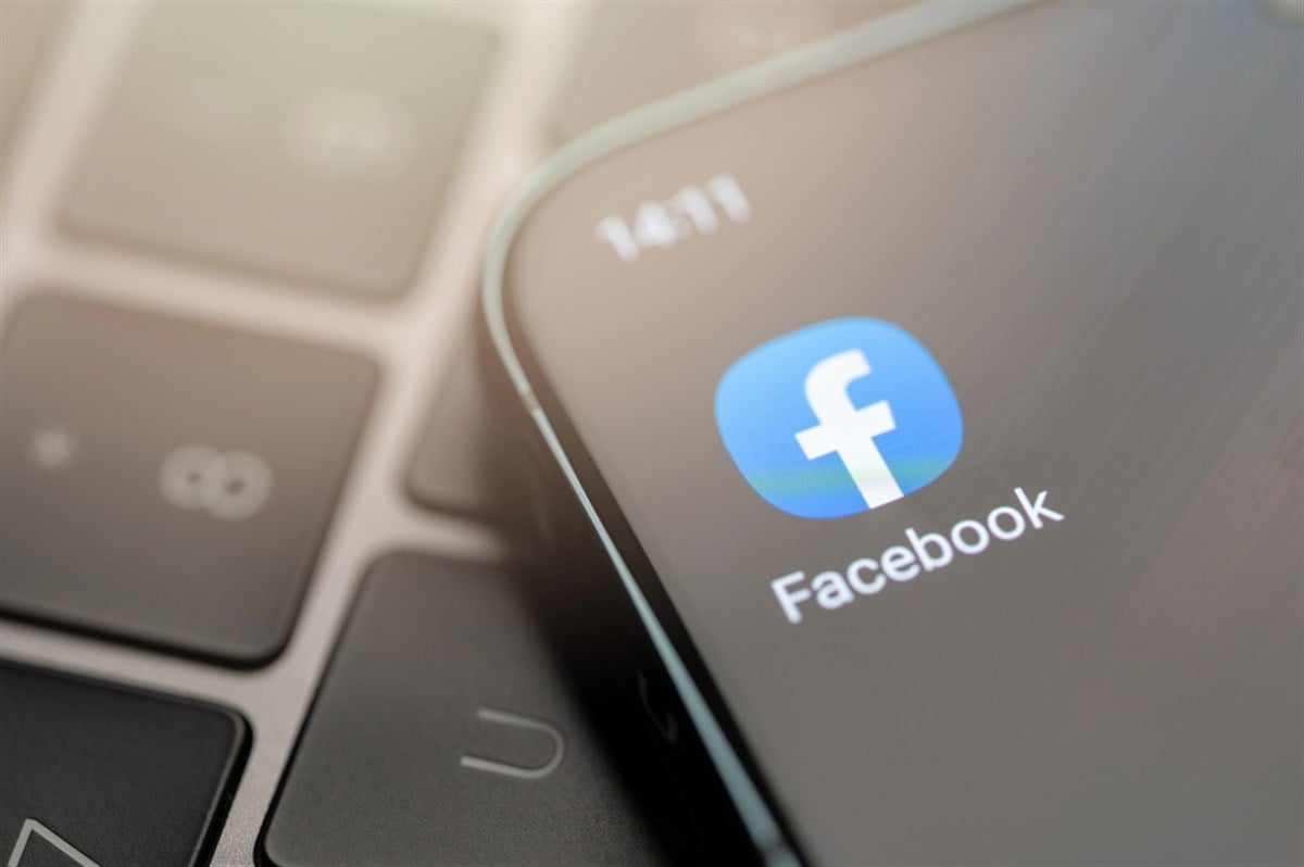 Facebook app on smartphone screen against laptop keyboard in background. 