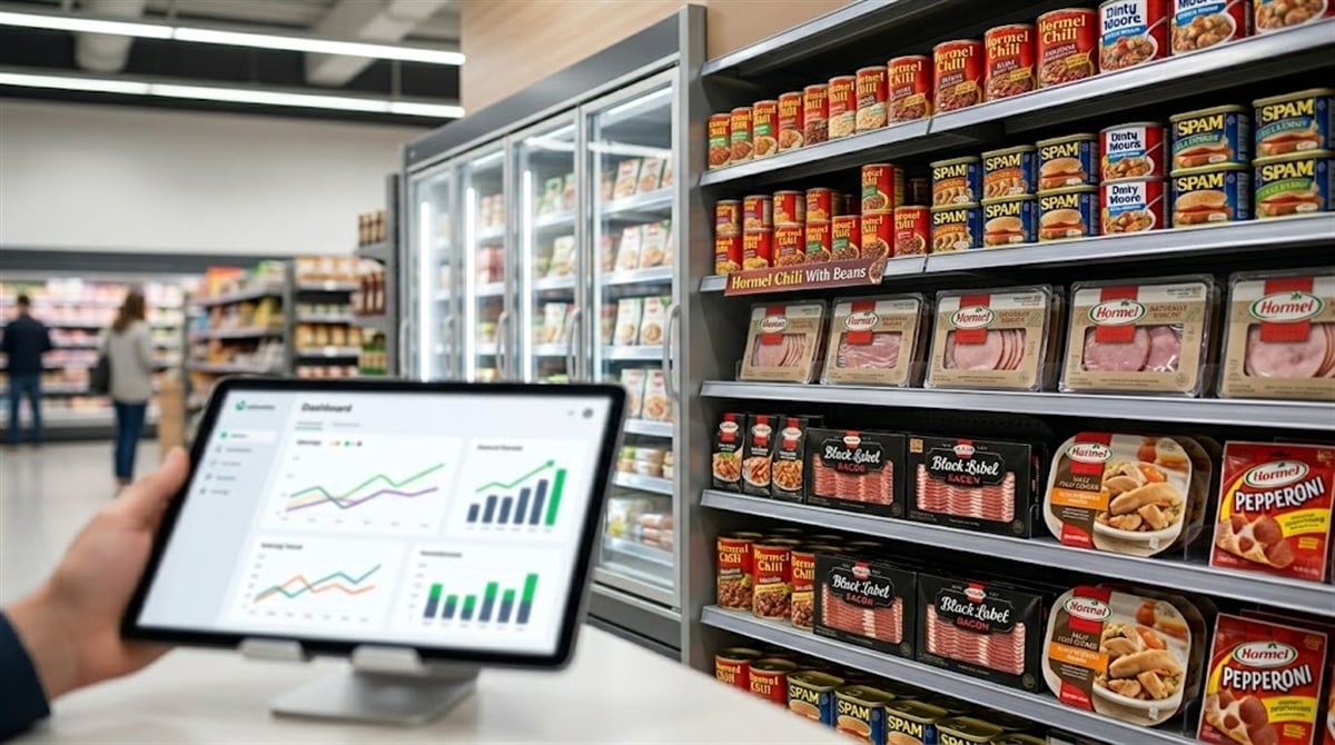 A tablet displaying a financial dashboard is held in front of a grocery store shelf stocked with Hormel Foods products including SPAM, Hormel Chili, Black Label Bacon, and Hormel Pepperoni.
