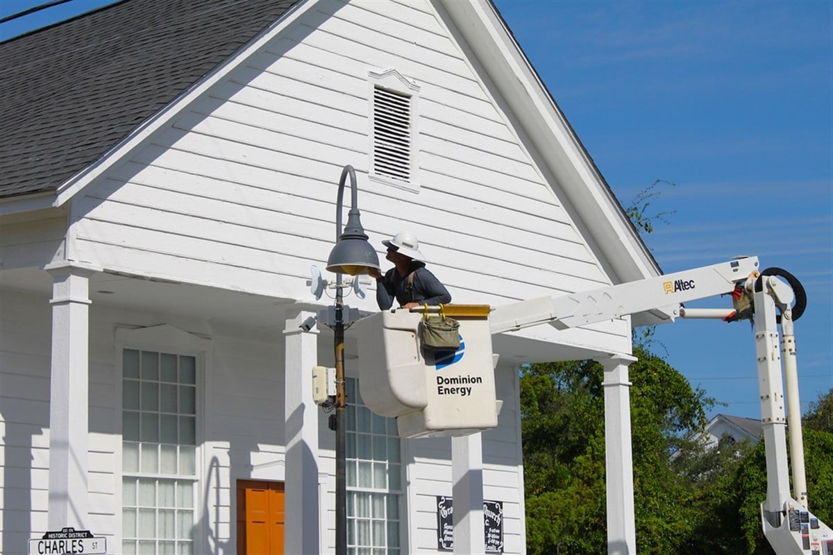Beaufort, SC, USA - September 25, 2024: Maintenance work done by worker of Dominion Energy. Inspection of streetlight. Craftsman on lifting platform with helmet. Front of white church building in back