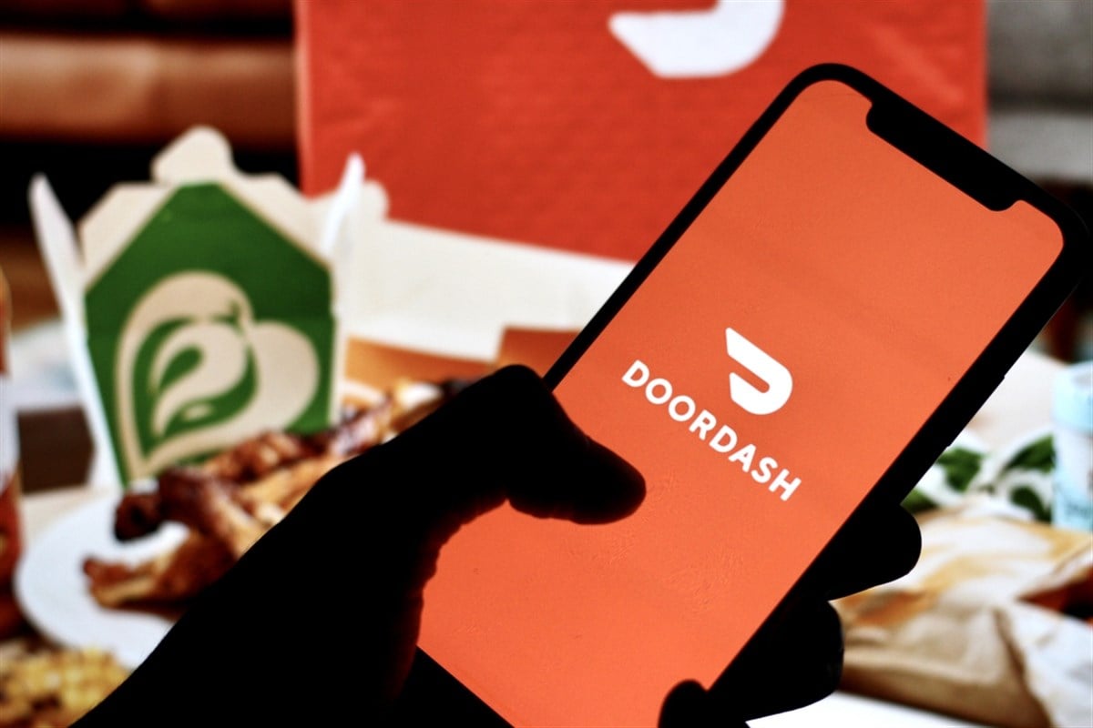 DoorDash logo on a mobile phone positioned in front of takeout containers.