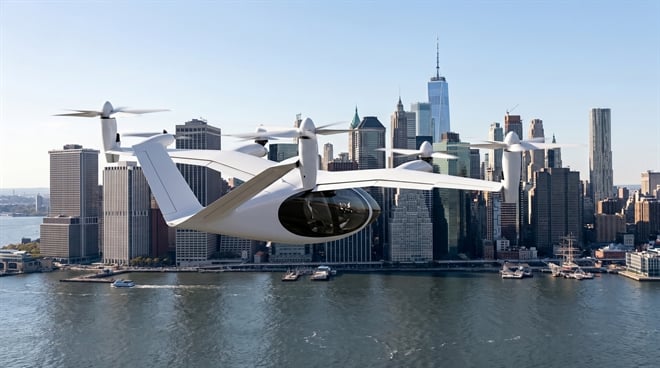 A white electric vertical takeoff and landing aircraft flies over a city skyline and waterway.