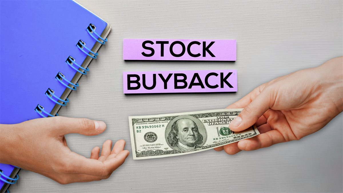 Hands exchange a $100 bill beneath “Stock Buyback” labels on a desk, illustrating corporate repurchase spending.