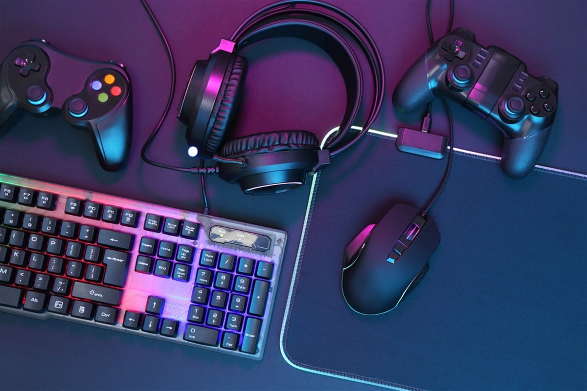 Computer mouse, RGB keyboard, headset and game controllers in neon lights on dark background, top view — Photo