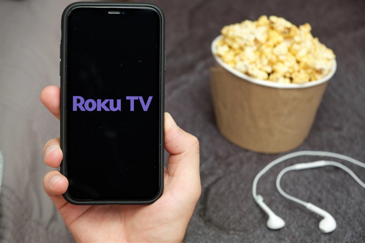 Roku logo on phone screen with popcorn and earbuds in the backdrop