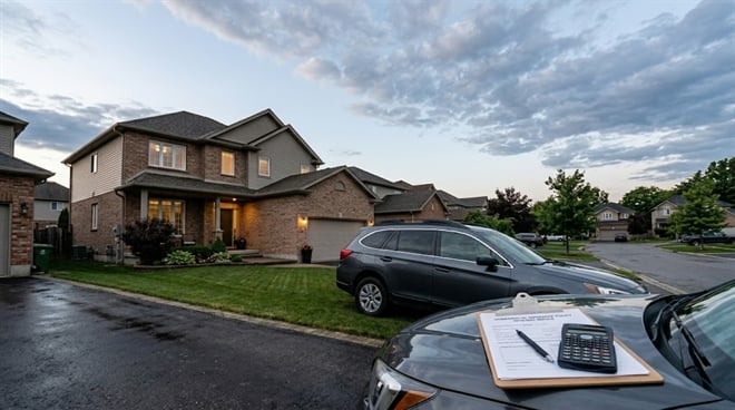 A suburban home at twilight with a clipboard of insurance papers and a calculator on a car’s hood.