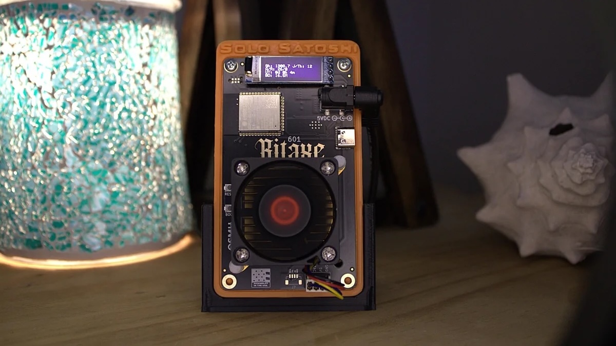 Orange and black solo Bitcoin mining machine sitting on a wood table.