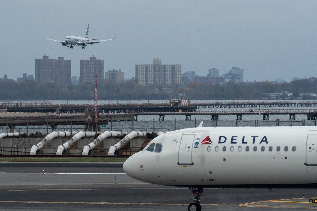 An American Airlines flight lands as a Delta Air Lines plane taxis at LaGuardia Airport (LGA) in the Queens borough of New York, Sunday, Nov. 9, 2025. (AP Photo/Adam Gray)