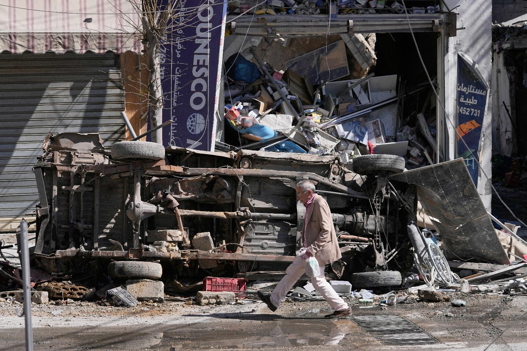 A man passes by a destroyed car and shop on a commercial street that was hit by Israeli airstrikes in Nabatiyeh town, south Lebanon, Thursday, March 5, 2026. (AP Photo/Mohammed Zaatari)