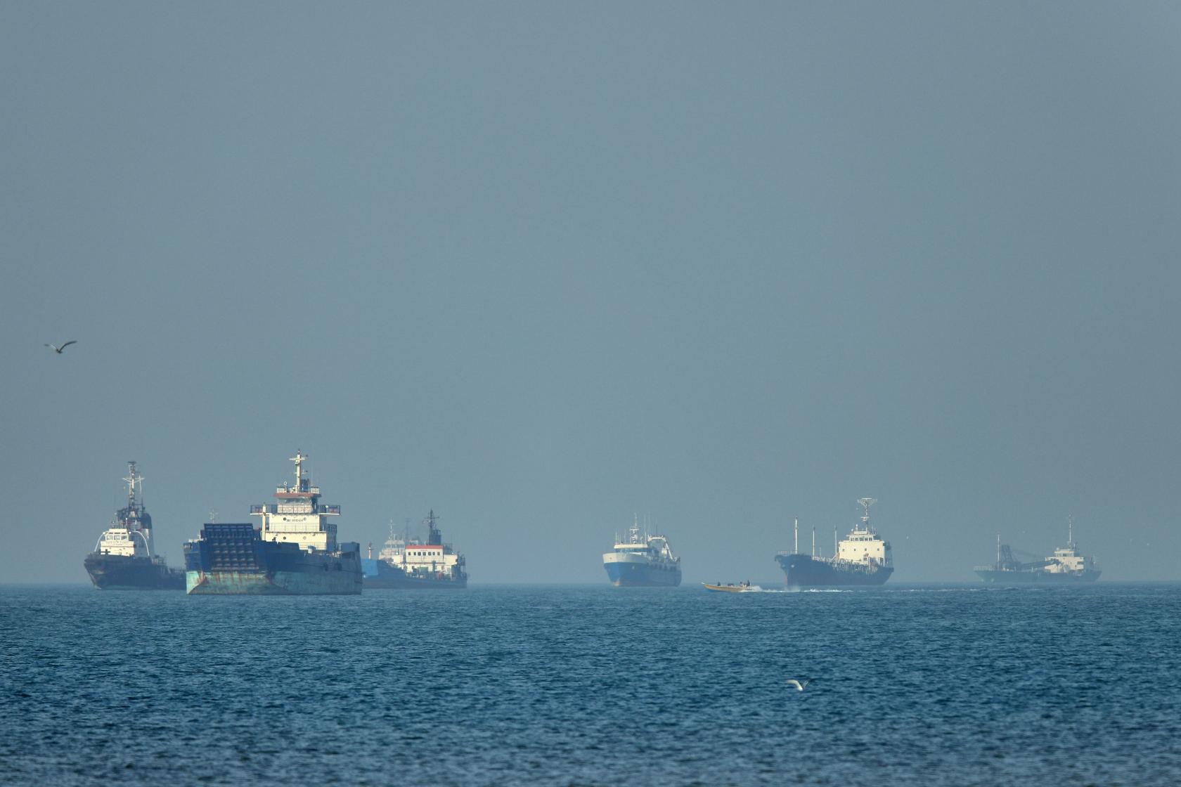 Cargo ships, including bulk carriers and general cargo vessels, sit at anchor offshore as a small motorboat passes in the foreground, in the Strait of Hormuz off Bandar Abbas, Iran, Monday, May 4 , 2026.(Amirhosein Khorgooi/ISNA via AP)