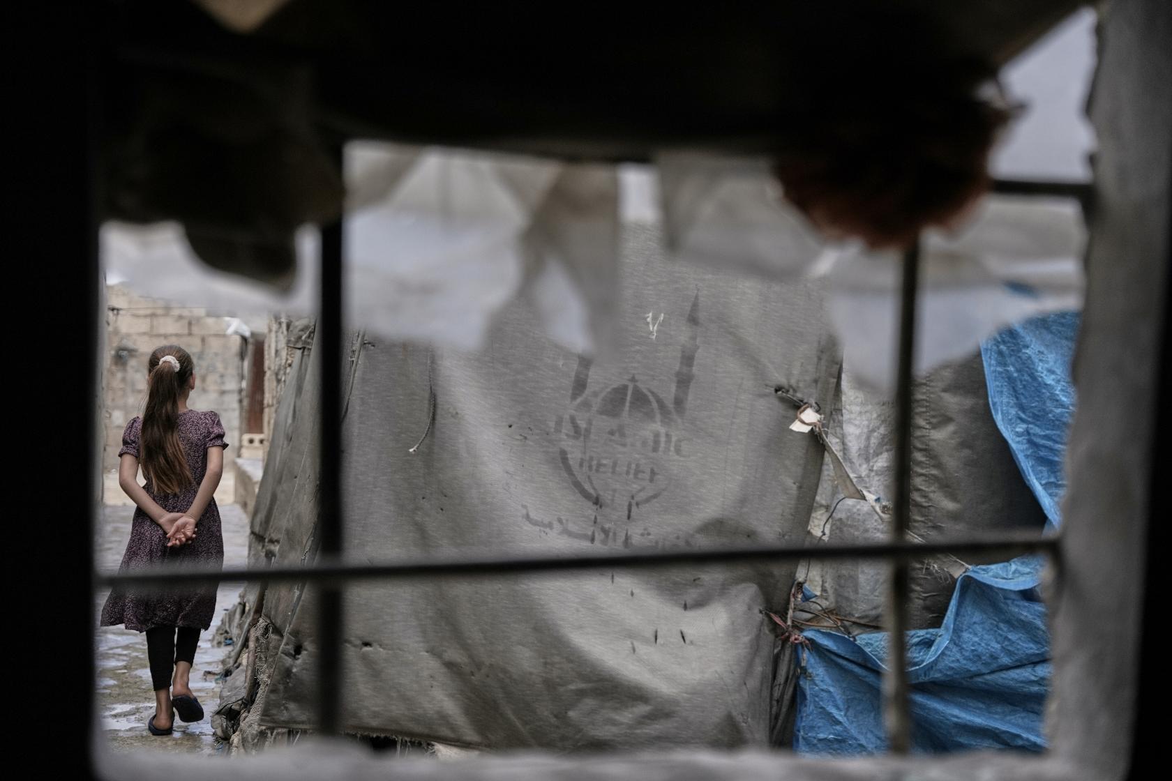 A girl walks through al-Karama camp, established in the early years of the Syrian conflict and built from scratch with light-brick structures covered with fabric to house internally displaced Syrians near the village of Atmeh, Idlib province, Syria, Tuesday, May 19, 2026. (AP Photo/Omar Albam)