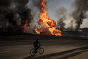 A man rides his bike past flames and smoke rising from a fire following a Russian attack in Kharkiv, Ukraine, Friday, March 25, 2022. (AP Photo/Felipe Dana)