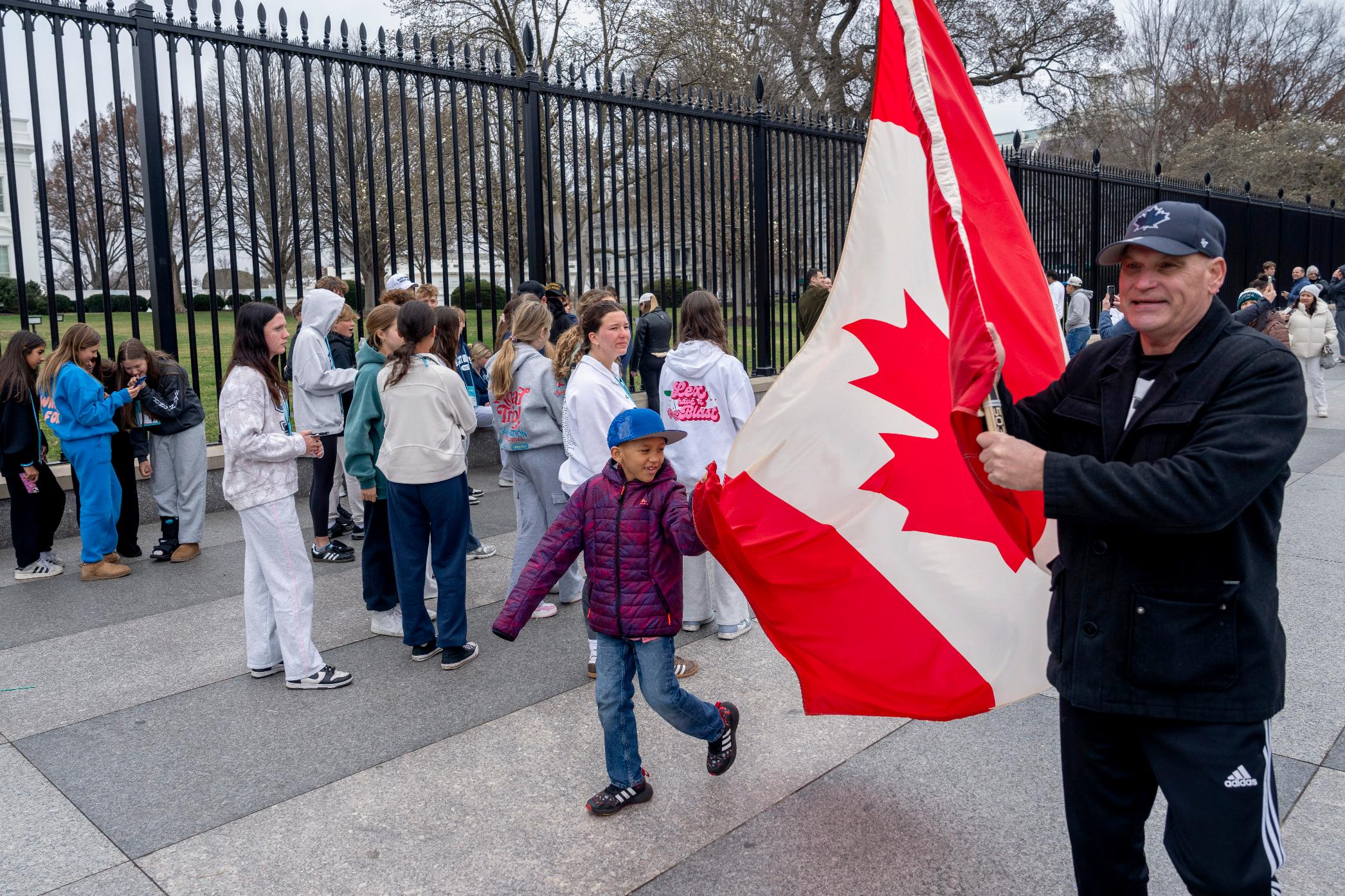 FILE - Toronto residents Douglas Bloomfield, from right, and his son Phoenix, who are on vacation in Washington, hold a Canadian flag and an ice hockey stick to show their support for Canada regarding trade tariffs, in front of the White House in Washington, March 13, 2025. (AP Photo/Ben Curtis, File)