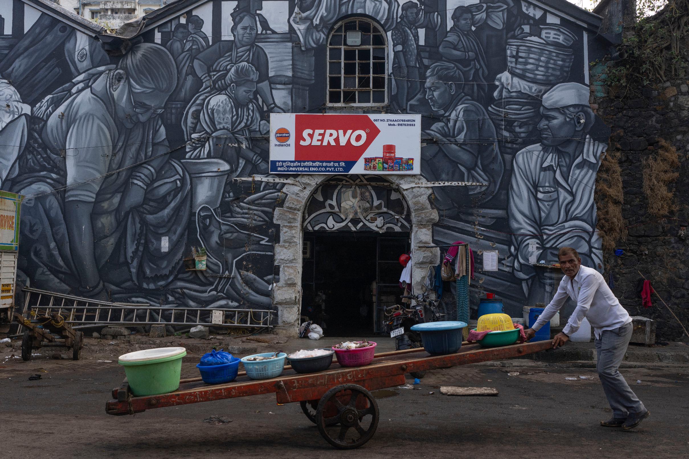 A fisherman pushes his cart filled with catch as he passes by a mural of the fisher community at Sassoon Dock In Mumbai, India, Wednesday, April 8, 2026. (AP Photo/Rafiq Maqbool)